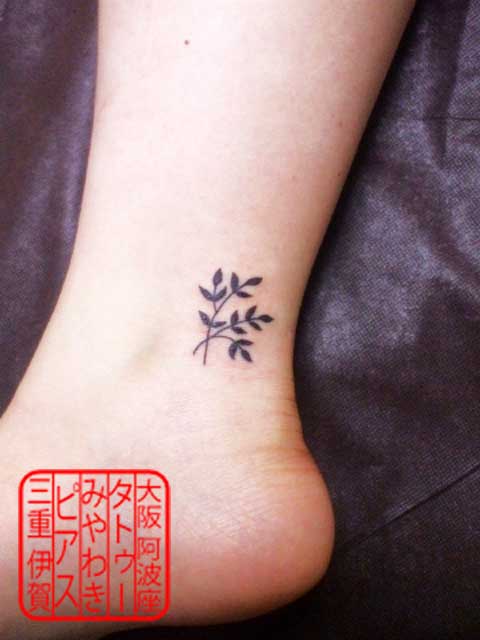 左足首外側のアキレス腱寄りに黒色で植物の葉が折り重なったデザインのワンポイントタトゥー