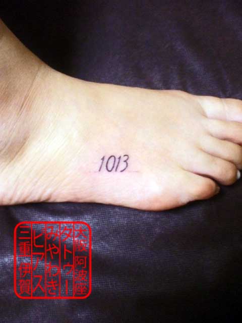 右足甲外側に黒い細い線でシンプルな書体での4つの数字の小さいタトゥー