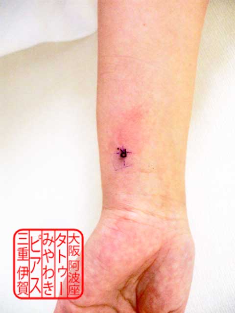 左手首内側に黒色での細い線で英文字のRを大文字でピリオドも付けたスモールサイズのタトゥー